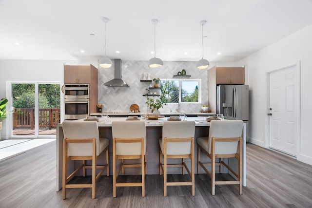 kitchen featuring pendant lighting, wall chimney exhaust hood, a wealth of natural light, and a kitchen bar