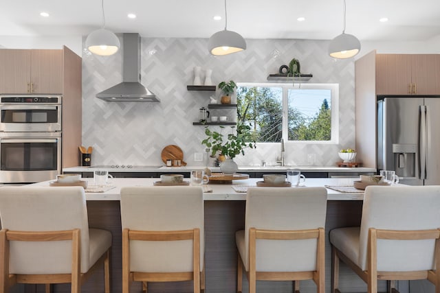 kitchen with light stone countertops, wall chimney range hood, decorative light fixtures, and stainless steel appliances