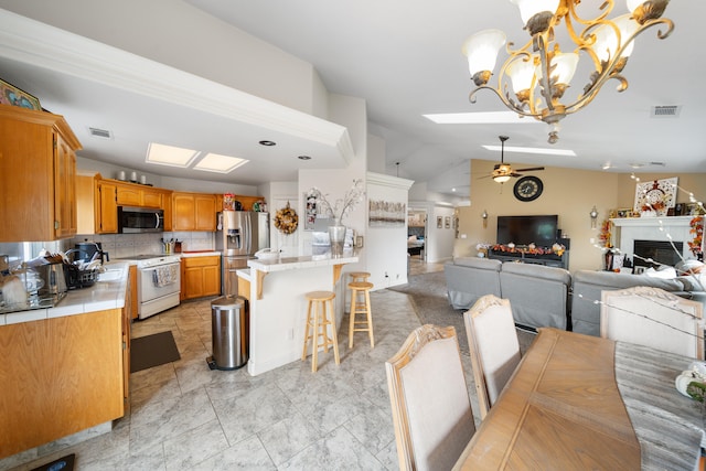 kitchen featuring hanging light fixtures, stainless steel appliances, backsplash, lofted ceiling, and ceiling fan with notable chandelier