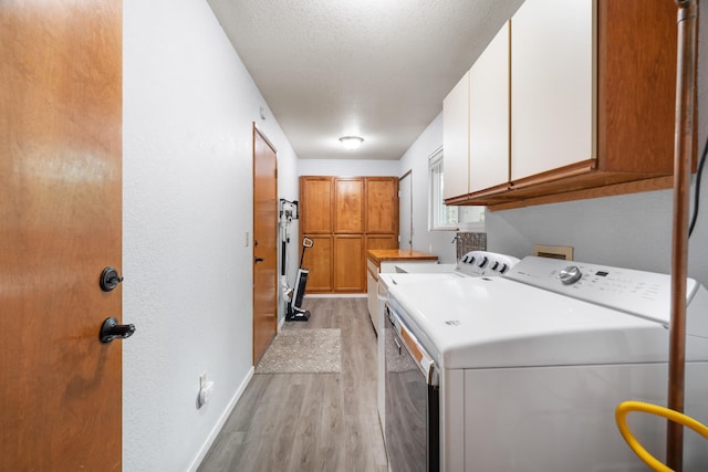 clothes washing area featuring a textured ceiling, washing machine and clothes dryer, light hardwood / wood-style floors, and cabinets