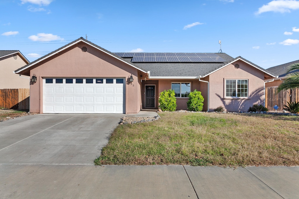 single story home featuring a front yard, solar panels, and a garage