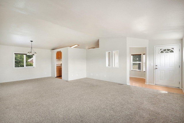 unfurnished living room with light carpet, lofted ceiling, and a notable chandelier