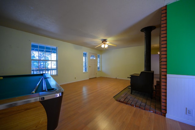 interior space with a wood stove, billiards, wood-type flooring, and ceiling fan