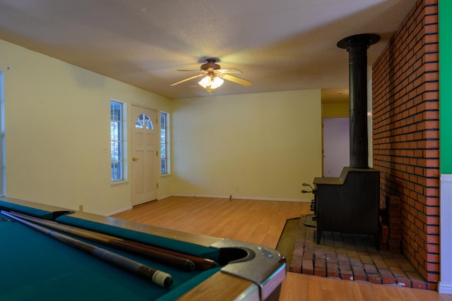 interior space with wood-type flooring, a wood stove, billiards, a textured ceiling, and ceiling fan