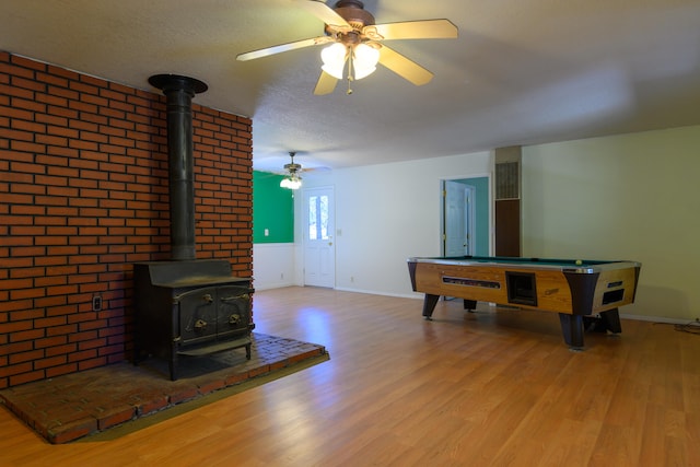 recreation room featuring light hardwood / wood-style flooring, a wood stove, billiards, a textured ceiling, and ceiling fan