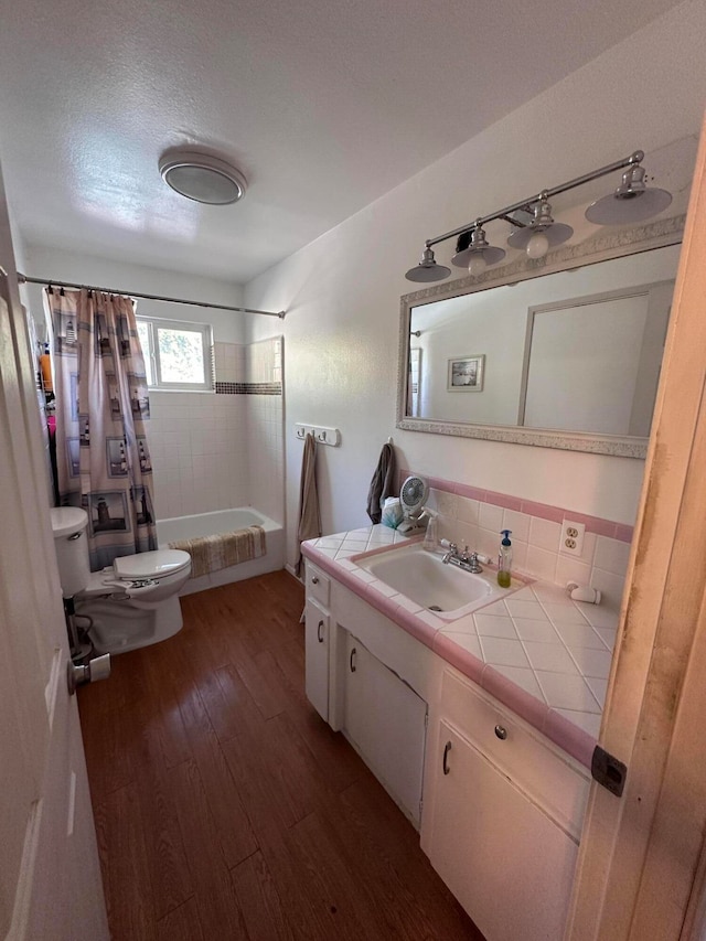 full bathroom featuring toilet, hardwood / wood-style floors, a textured ceiling, vanity, and shower / tub combo