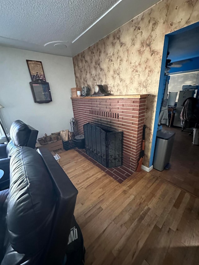 living room with hardwood / wood-style floors, ceiling fan, a textured ceiling, and a brick fireplace