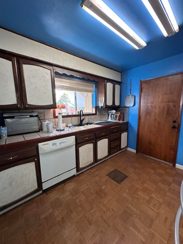 kitchen with tile countertops, white dishwasher, dark parquet floors, sink, and dark brown cabinets