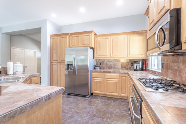 kitchen featuring tile counters, sink, backsplash, appliances with stainless steel finishes, and light brown cabinetry