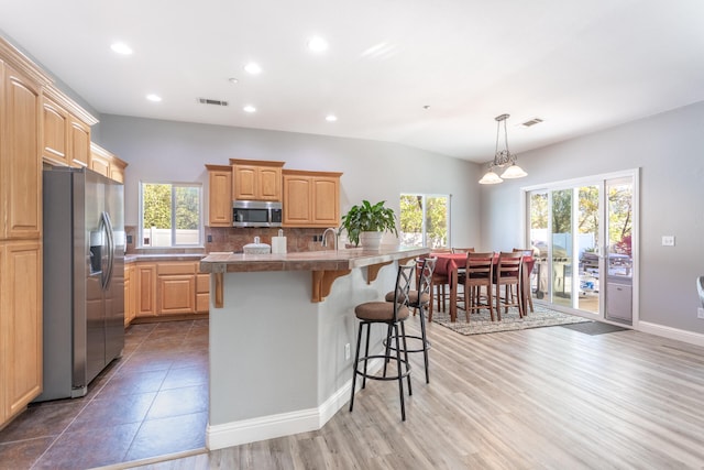 kitchen with appliances with stainless steel finishes, tasteful backsplash, a kitchen bar, hardwood / wood-style floors, and a kitchen island with sink