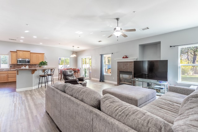 living room featuring light hardwood / wood-style flooring, ceiling fan, and a tile fireplace