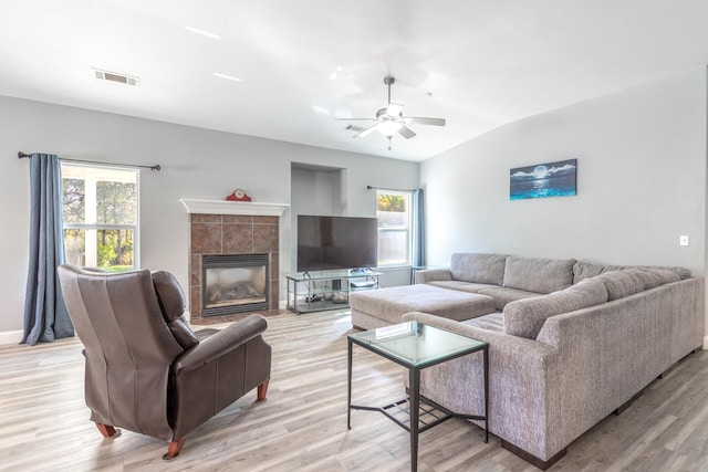 living room with light hardwood / wood-style floors, a tiled fireplace, a healthy amount of sunlight, and vaulted ceiling