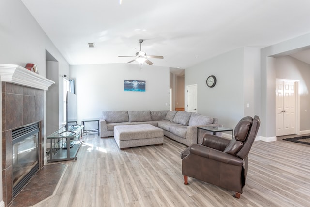 living room featuring light hardwood / wood-style floors, lofted ceiling, ceiling fan, and a tile fireplace