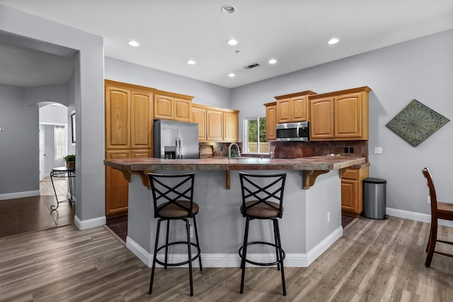 kitchen featuring an island with sink, dark countertops, arched walkways, a kitchen bar, and appliances with stainless steel finishes