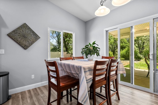dining space featuring lofted ceiling, light wood finished floors, and baseboards