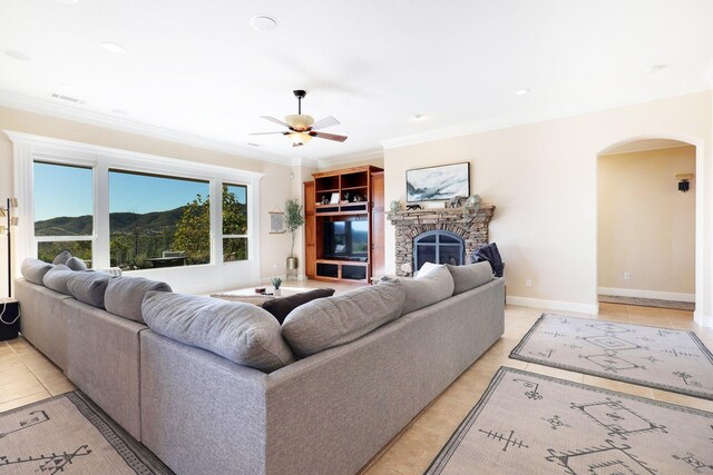 living room featuring a stone fireplace, ceiling fan, light tile patterned floors, and ornamental molding