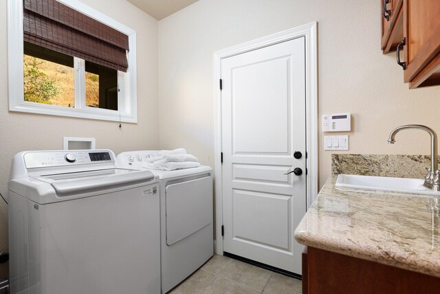 clothes washing area with washing machine and dryer, sink, light tile patterned flooring, and cabinets