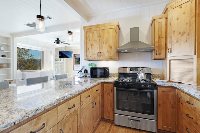 kitchen with gas stove, wall chimney range hood, light stone counters, light hardwood / wood-style flooring, and pendant lighting