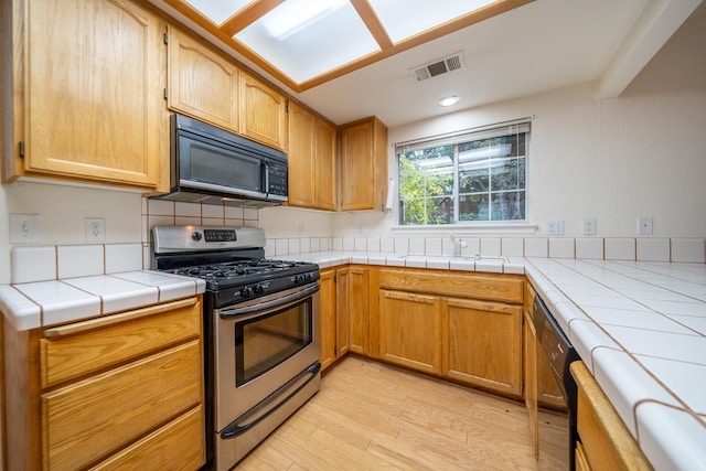 kitchen featuring backsplash, tile countertops, black appliances, and light wood-type flooring