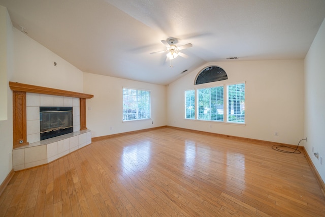 unfurnished living room with ceiling fan, vaulted ceiling, a tile fireplace, and light hardwood / wood-style flooring