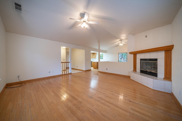 unfurnished living room with ceiling fan, light hardwood / wood-style flooring, a tile fireplace, and vaulted ceiling