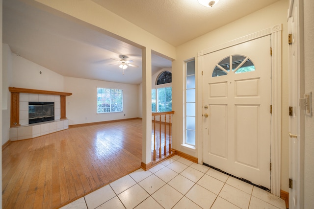 foyer with a textured ceiling, ceiling fan, a tile fireplace, light hardwood / wood-style flooring, and lofted ceiling