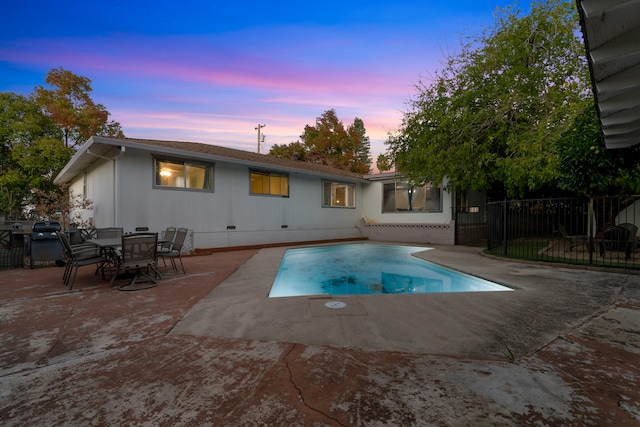 pool at dusk with a patio and area for grilling