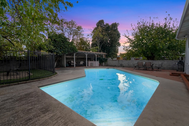 pool at dusk with a patio area and grilling area