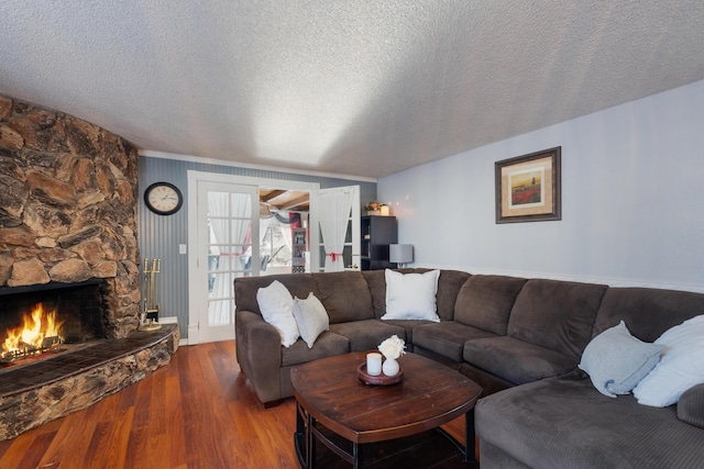 living room featuring a stone fireplace, a textured ceiling, and hardwood / wood-style floors