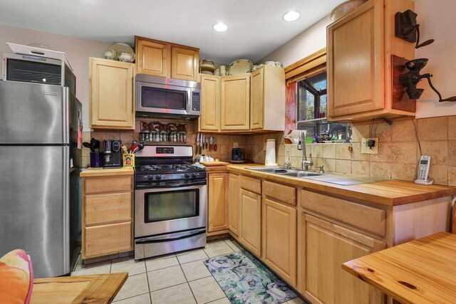 kitchen with butcher block counters, sink, appliances with stainless steel finishes, light tile patterned floors, and decorative backsplash
