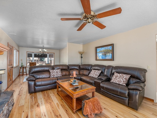 living room featuring light hardwood / wood-style floors, ceiling fan with notable chandelier, and a textured ceiling