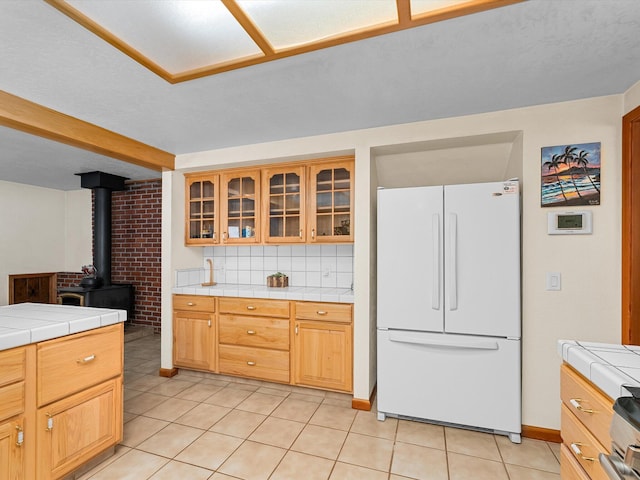 kitchen featuring white fridge, backsplash, light tile patterned floors, light brown cabinets, and tile countertops