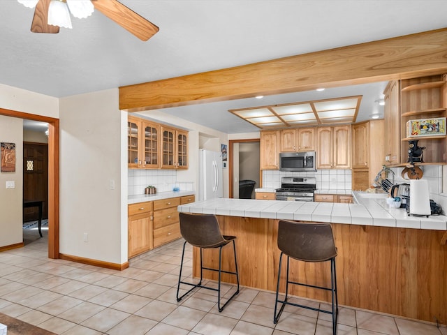 kitchen with tile counters, stainless steel appliances, decorative backsplash, kitchen peninsula, and a breakfast bar