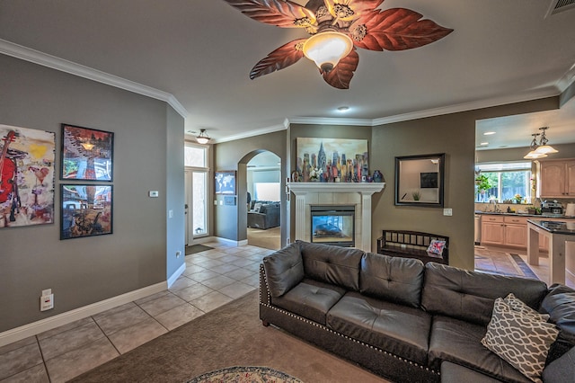 tiled living room with ceiling fan, a tiled fireplace, sink, and crown molding