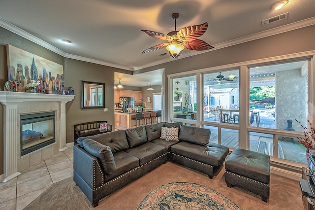 tiled living room with ceiling fan, a tile fireplace, and crown molding