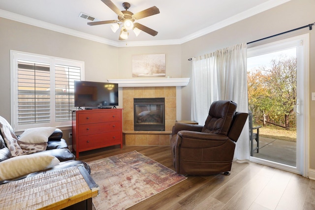 living room with ceiling fan, wood-type flooring, crown molding, and a tile fireplace