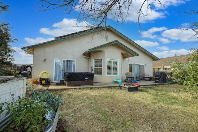 back of property with a fire pit, a hot tub, a patio area, and a lawn