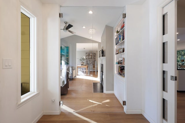 hall featuring built in shelves, light hardwood / wood-style floors, and lofted ceiling