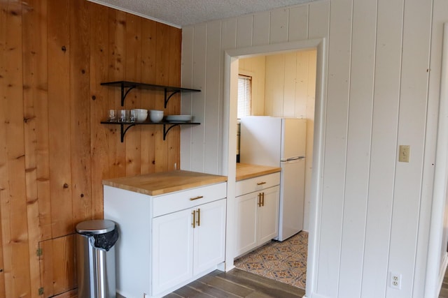 kitchen with wood counters, wood walls, a textured ceiling, white refrigerator, and white cabinets