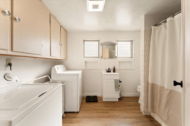 clothes washing area with sink, washing machine and clothes dryer, and light hardwood / wood-style floors