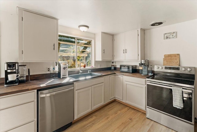 kitchen with stainless steel appliances, light hardwood / wood-style floors, sink, white cabinets, and wood counters