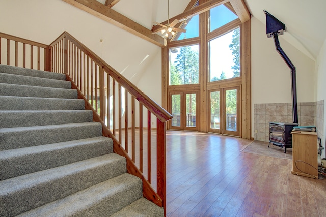 stairway with beam ceiling, a wood stove, high vaulted ceiling, tile walls, and hardwood / wood-style flooring