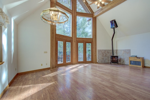 unfurnished living room featuring a wood stove, french doors, high vaulted ceiling, ceiling fan with notable chandelier, and hardwood / wood-style flooring