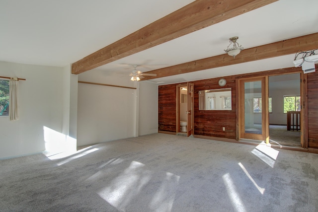 unfurnished living room with carpet flooring, beam ceiling, ceiling fan, and wooden walls