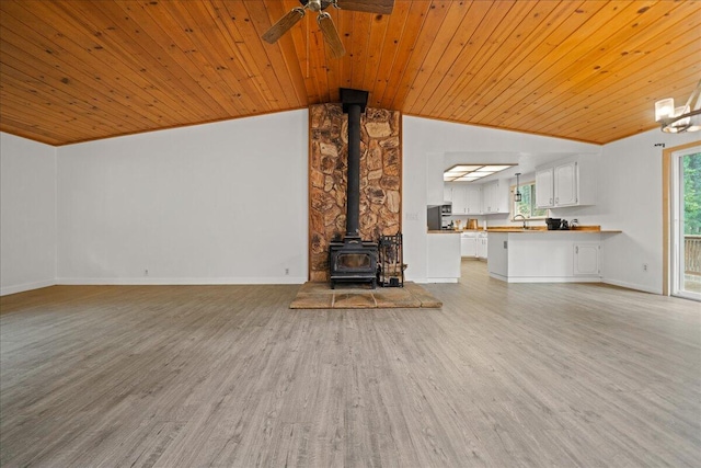 unfurnished living room with light hardwood / wood-style floors, wood ceiling, a wood stove, and vaulted ceiling