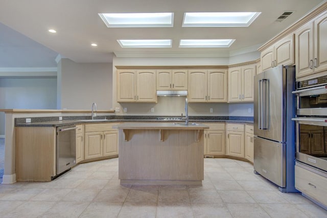 kitchen featuring a center island with sink, light brown cabinets, ornamental molding, and appliances with stainless steel finishes