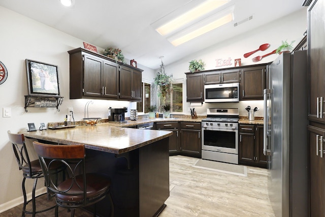 kitchen with lofted ceiling with skylight, light hardwood / wood-style floors, a kitchen bar, kitchen peninsula, and stainless steel appliances