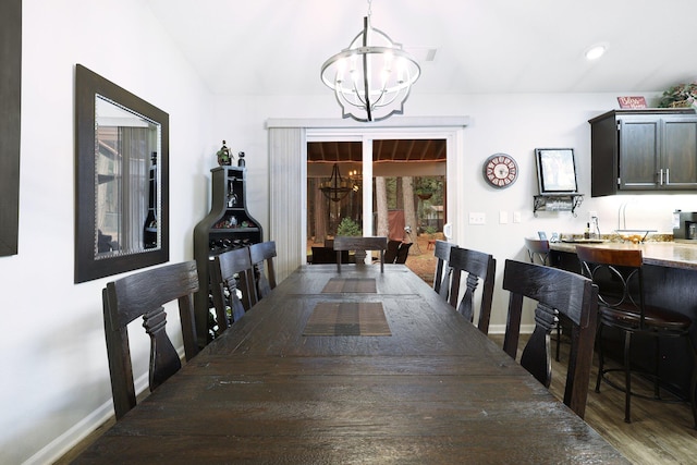 dining space with wood-type flooring, vaulted ceiling, and a notable chandelier