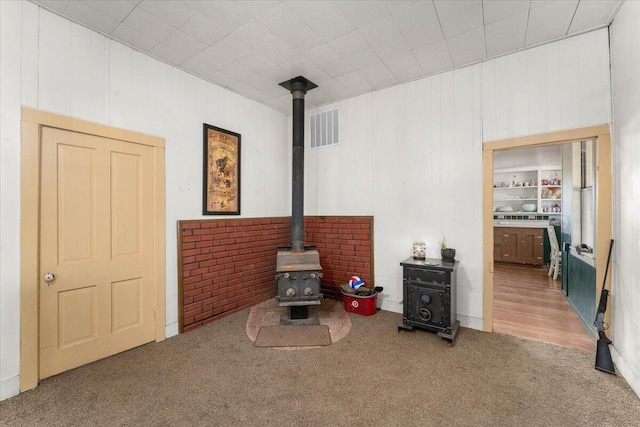 sitting room with a wood stove, wood walls, built in features, and carpet