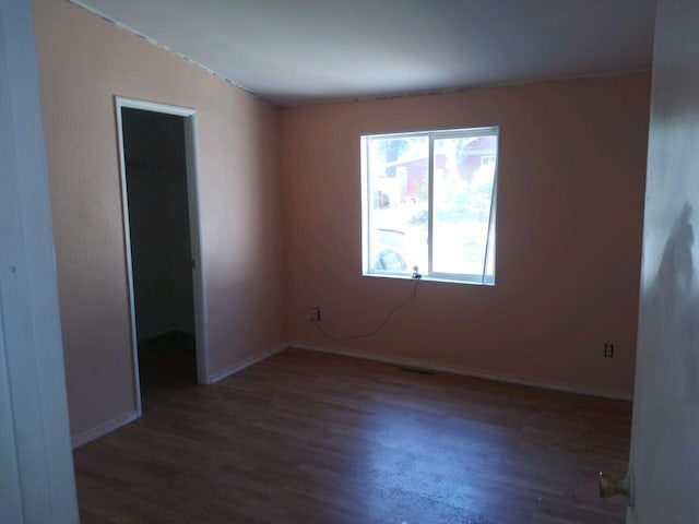 empty room with dark hardwood / wood-style flooring and vaulted ceiling